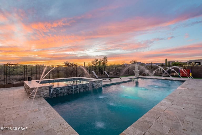 Luxury backyard pool at sunset with turquoise water, white lounge chairs, and dramatic pink-orange sky over distant city skyline